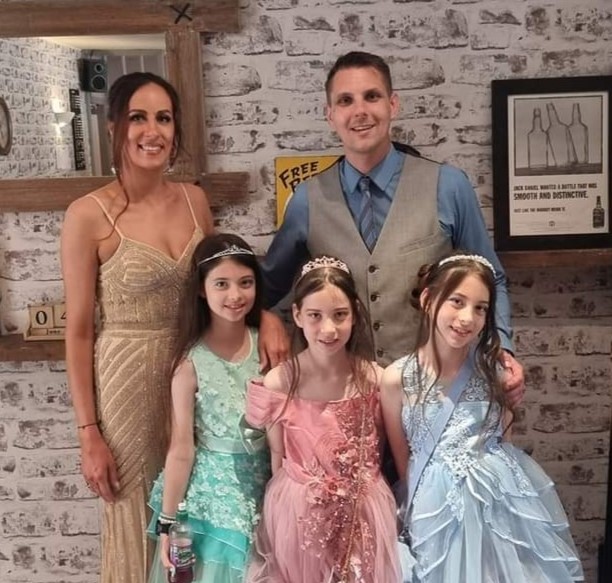 Image shows Helen with her husband and three daughters in formal dress attire.
